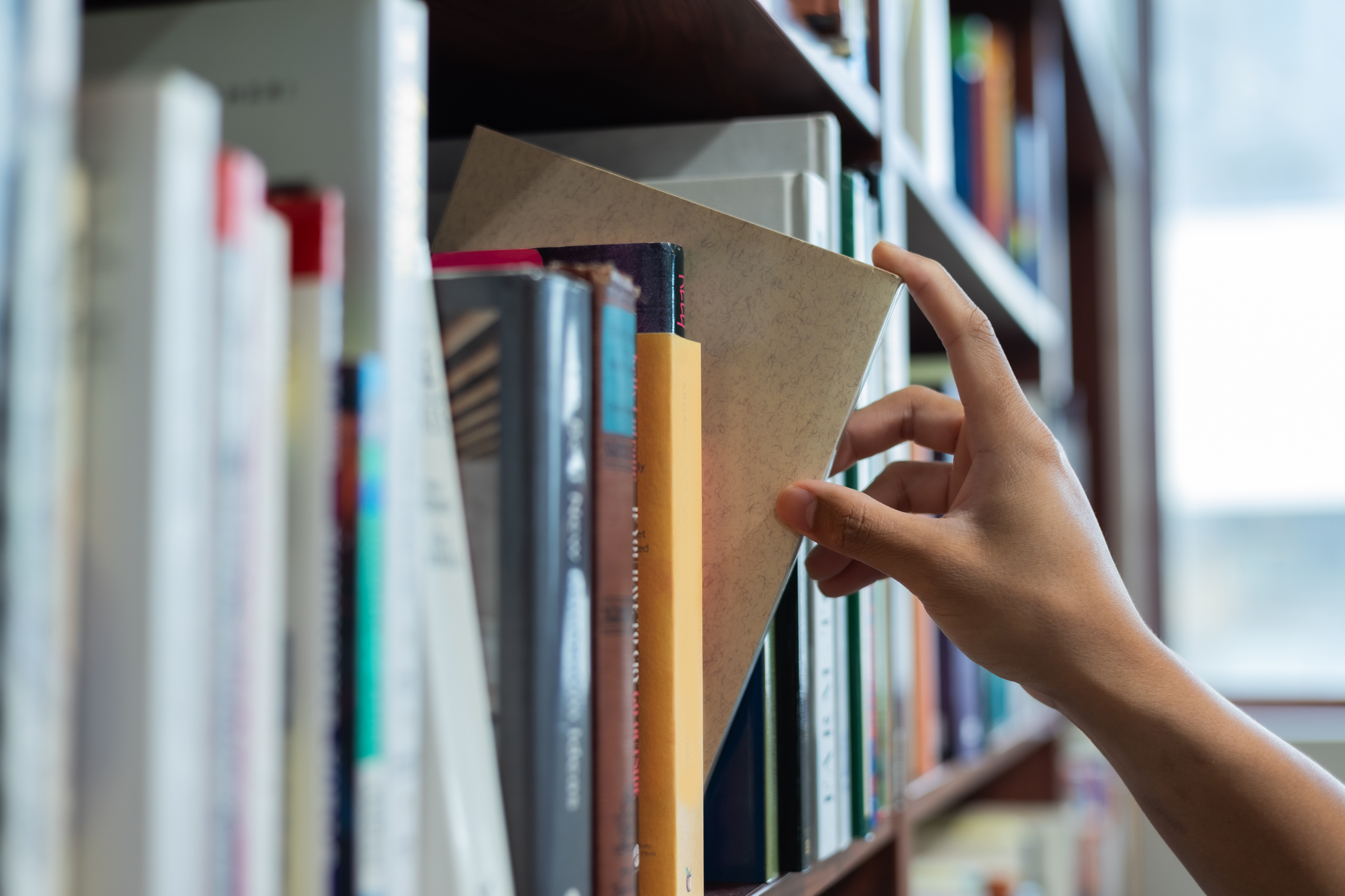 Hand pulling a book from a library shelf, symbolising research, academic reading, and careful engagement with scholarship.