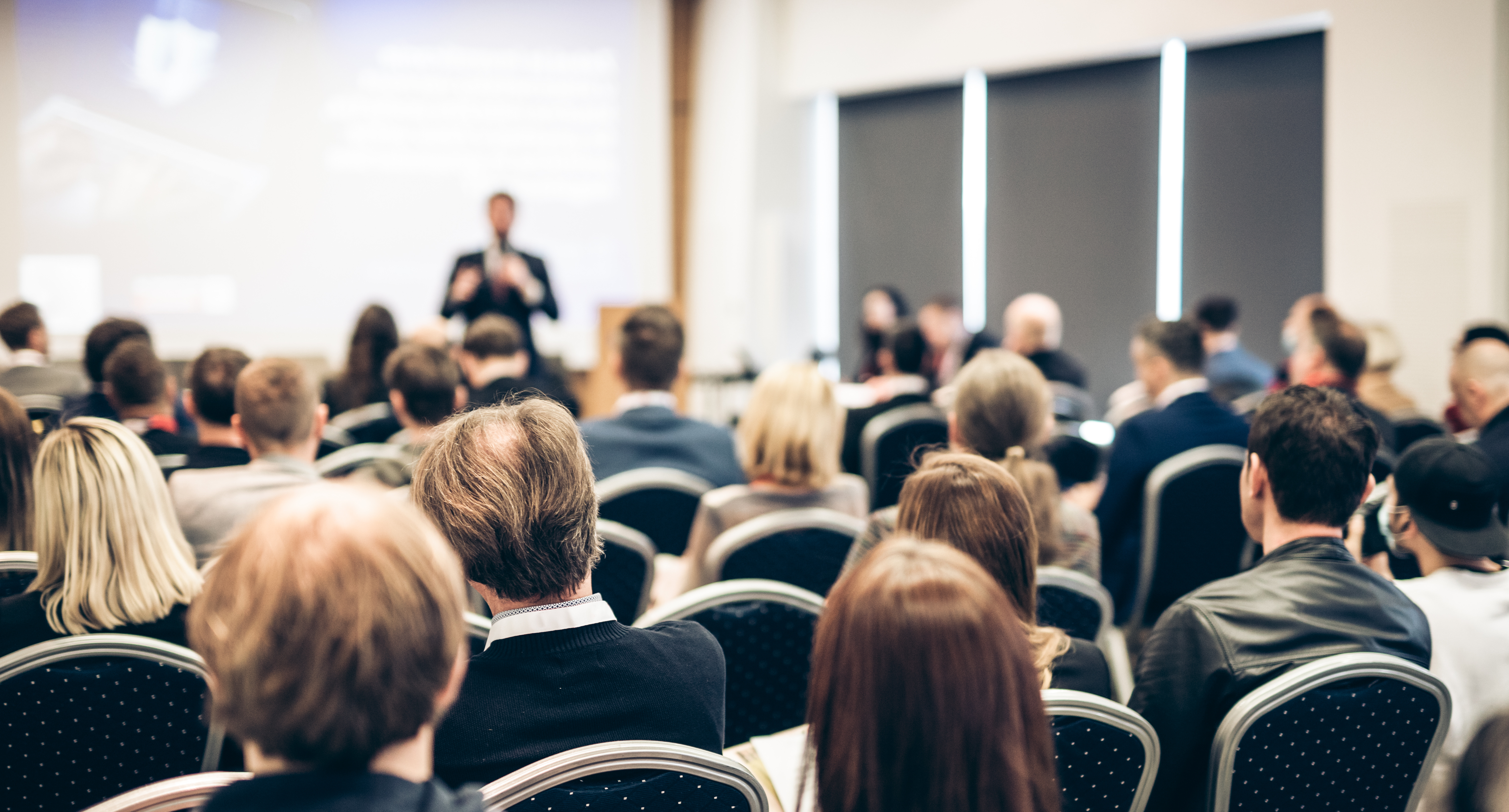 Audience listening to a speaker during an academic conference presentation in a modern conference hall.