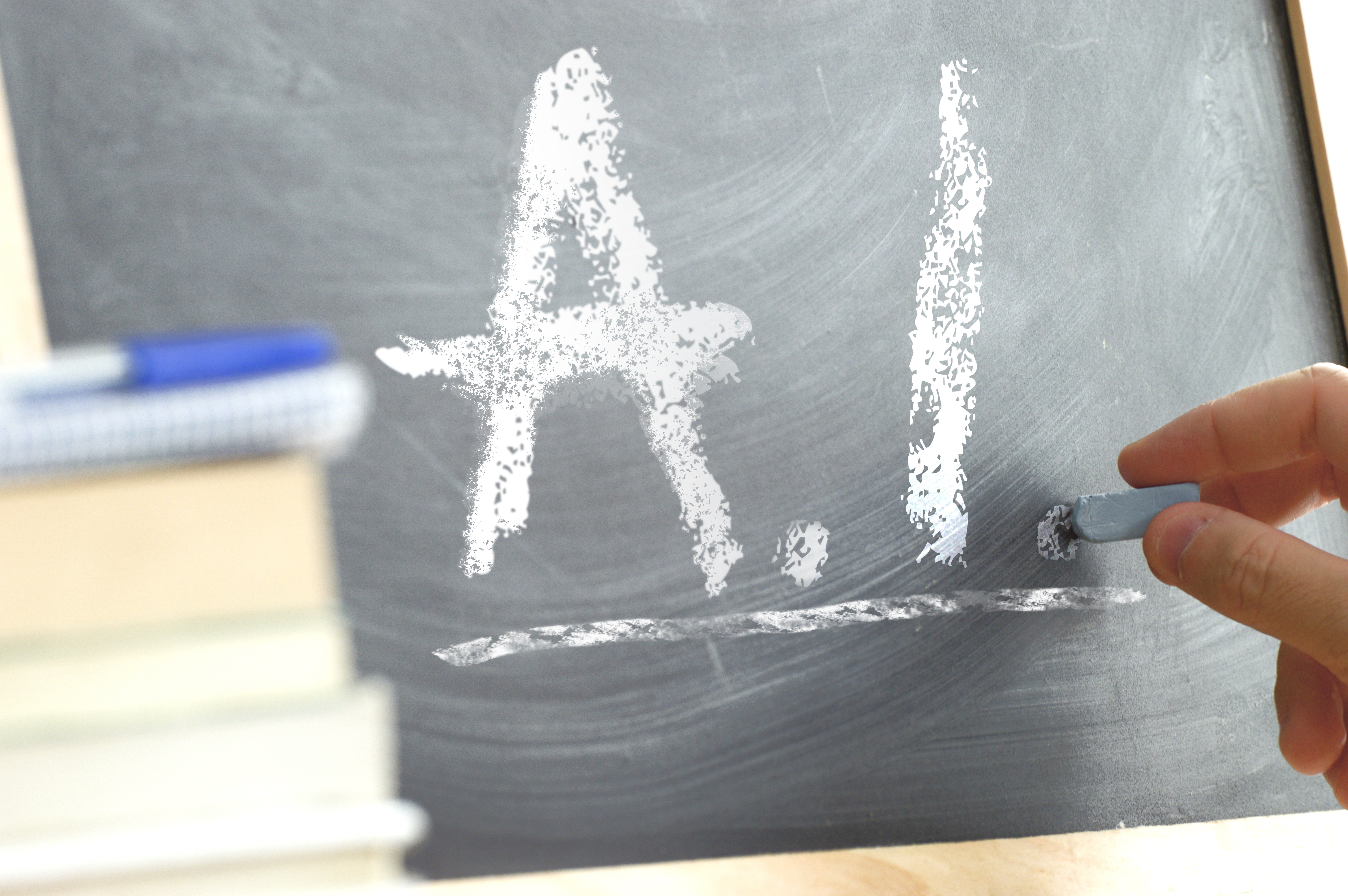 Hand writing A.I. with chalk on a classroom blackboard beside books, representing thoughtful AI use in language education.