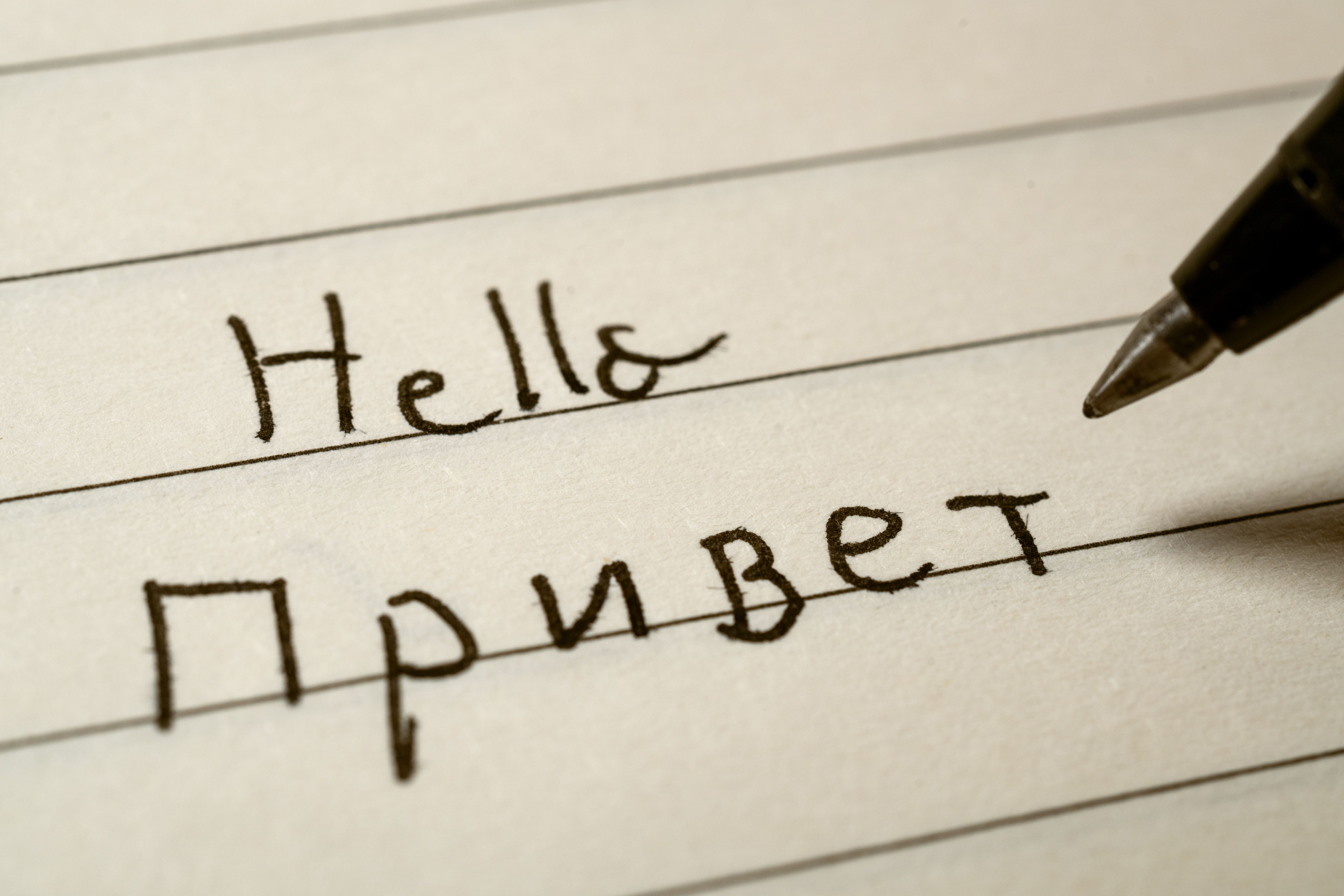 “Handwritten ‘Hello’ in English and Russian on lined paper, illustrating the challenges Russian speakers face when learning Greek