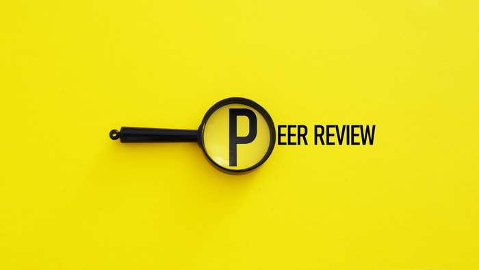 Magnifying glass enlarging the letter P in the words "peer review" printed on a yellow background